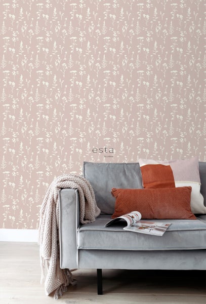 Szene mit floral gemusterter Tapete hinter einem grauen Sofa mit Kissen und Decke