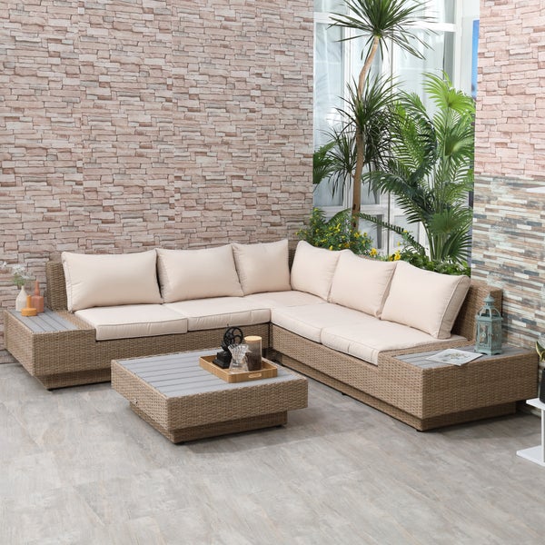 Modernes Ecksofa aus Polyrattan mit Textilauflagen und quadratischem Couchtisch in einem hellen Außenbereich mit Steinmauer und Pflanzen.