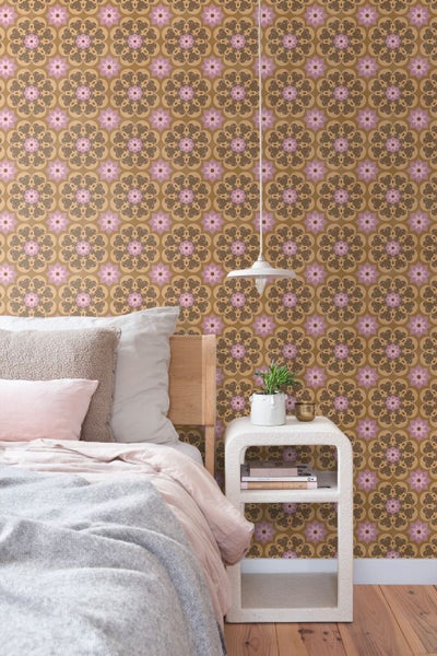 Schlafzimmer mit geometrischer Tapete im Blumendesign, Holzbett, weißem Nachttisch und Pendelleuchte.