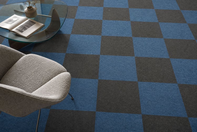 Teppichfliesen in einem Schachbrettmuster aus blauen und grauen Quadraten in einem modern eingerichteten Zimmer mit Sessel und Glastisch.