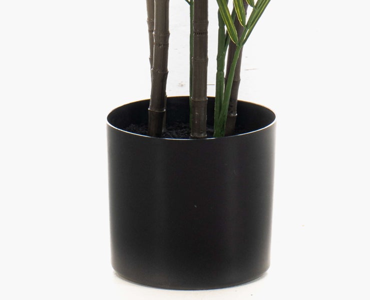 Künstliche Pflanze mit Bambusstämmen in einem schwarzen zylindrischen Kunststofftopf.