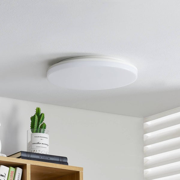 Runde weiße LED-Deckenleuchte montiert an einer weißen Decke in einem hellen Raum mit einem Holzregal und Kaktus.