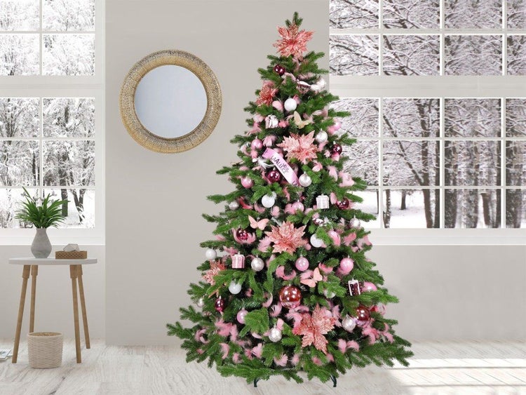 Künstlicher Weihnachtsbaum festlich geschmückt mit Kugeln Blumen und Bändern in einem weihnachtlich dekorierten Wohnzimmer mit Blick auf Winterwald
