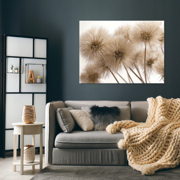 Modernes Wohnzimmer mit grauem Sofa, kuscheligen Kissen, weißem Beistelltisch und großem Wandbild mit Pusteblumen auf einer dunkelgrauen Wand.