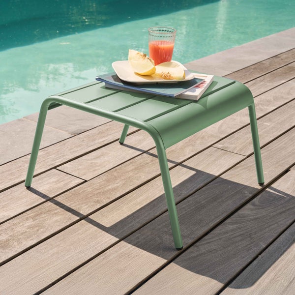 Kleiner grüner Beistelltisch aus Metall mit Lattenoberfläche auf einer Holzterrasse an einem Pool.