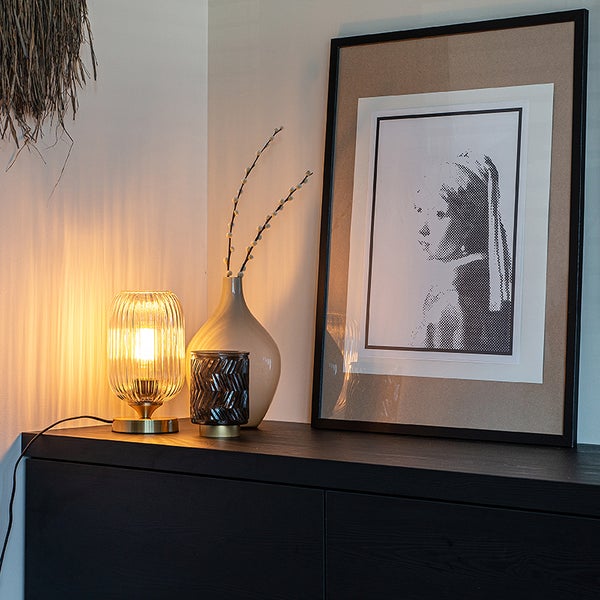 Dekorative Szene mit Tischleuchte, Vase, Windlicht und gerahmtem Bild auf einem schwarzen Sideboard