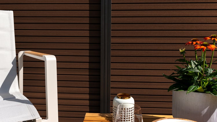 Szene mit Gartenmöbeln, Zaunelementen und Topfpflanze auf einer hellen Terrasse.