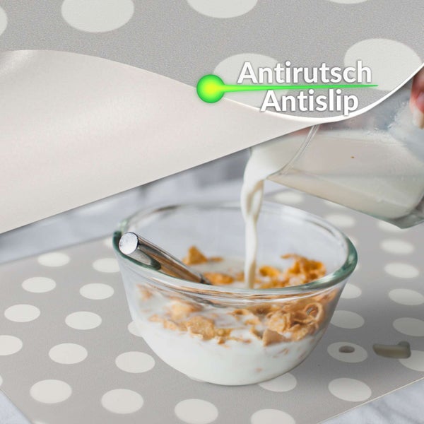 Nahaufnahme einer Antirutschmatte mit Punktmuster auf grauem Grund, auf der eine Glasschale mit Müsli und Milch steht.