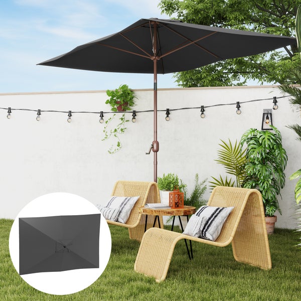 Rechteckiger Sonnenschirm in Anthrazit auf einer Terrasse mit zwei Rattansesseln, Holztisch und Lichterkette vor einer weißen Wand.