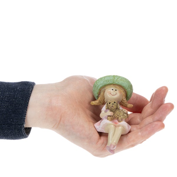 Kleine Dekofigur eines sitzenden Mädchens mit Hut und kleinem Tier im Arm, präsentiert in einer Hand zur Veranschaulichung der Größe.