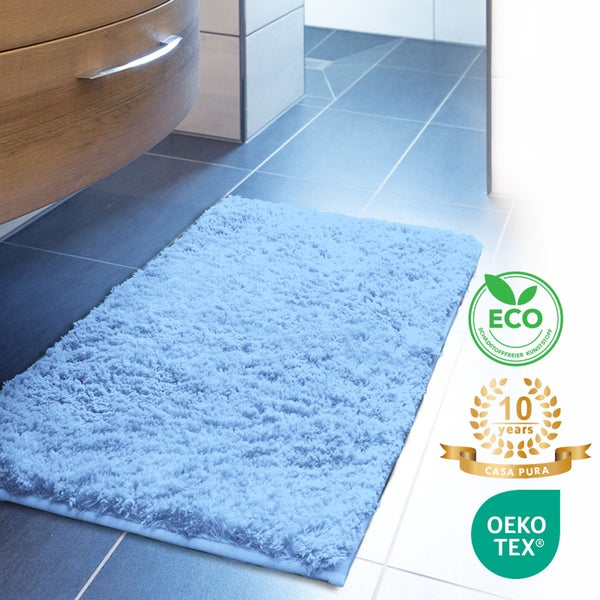 Blauer Badteppich aus Kunstfaser vor einem Waschtischunterschrank mit den Logos ECO, 10 Jahre Casa Pura und OEKO-TEX