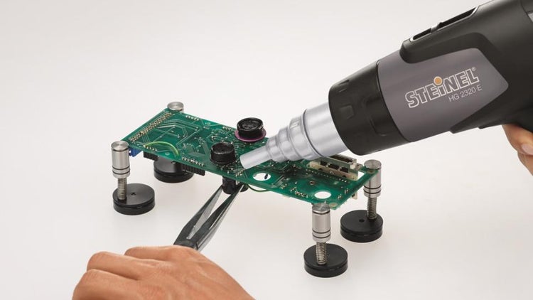 Heißluftgebläse Steinel HG 2320 E bei der präzisen Bearbeitung einer Platine mit Reduzierdüse und Flachzange.