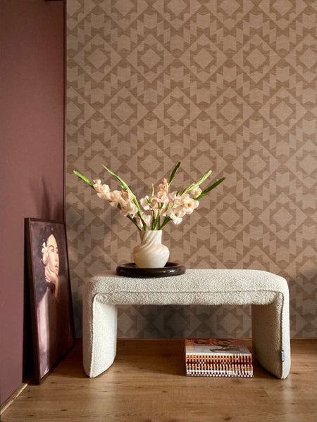 Wohnraum mit Vliestapete mit geometrischem Muster, davor steht eine Bank mit Blumen in einer Vase auf einem Holzboden.