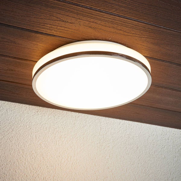 Runde, flache LED-Deckenleuchte mit Metallrahmen, montiert an einer dunklen Holzdecke neben einer weiß verputzten Wand.