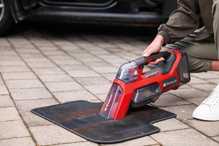 Einhell Akku Textilreiniger beim Reinigen einer Fußmatte vor einem Auto.