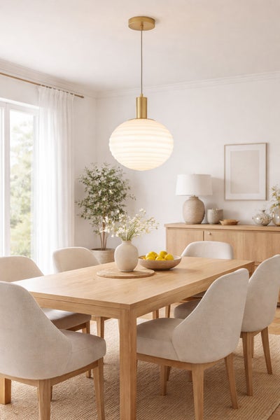 Helles Esszimmer mit Esstisch aus Holz, beigefarbenen Polsterstühlen und einer großen, gerippten Glas-Pendelleuchte mit Messingdetails.