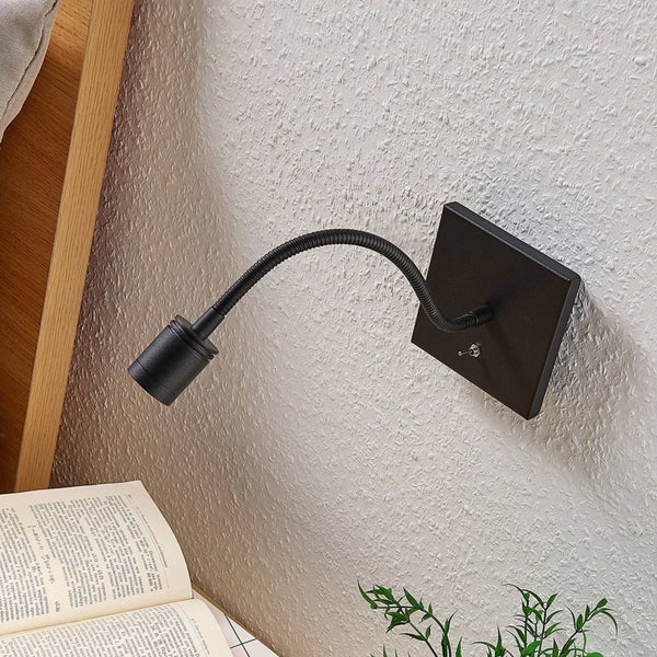 Schwarze Wandleseleuchte mit flexiblem Arm und Kippschalter an der quadratischen Basis, montiert über einem aufgeschlagenen Buch.