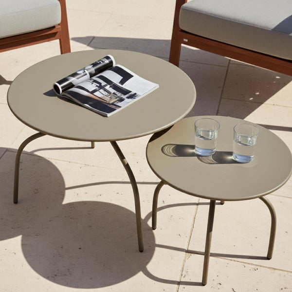 Zwei runde Beistelltische aus Metall in verschiedenen Größen auf einer Terrasse, mit einer Zeitschrift und zwei Gläsern Wasser.