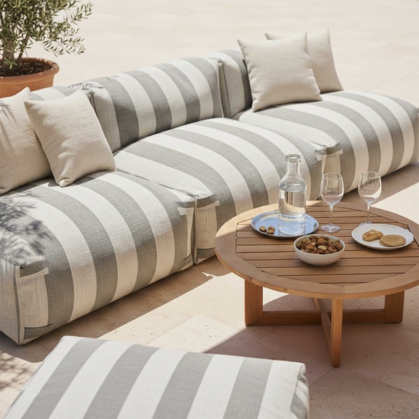 Gestreiftes Outdoor-Sofa mit hellen Kissen und rundem Holztisch auf einer hellen Terrasse.