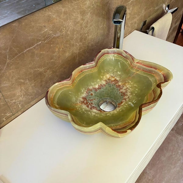 Aufsatzwaschbecken aus Naturstein in Blumenform mit verchromter Armatur auf weißem Waschtisch im Badezimmer.