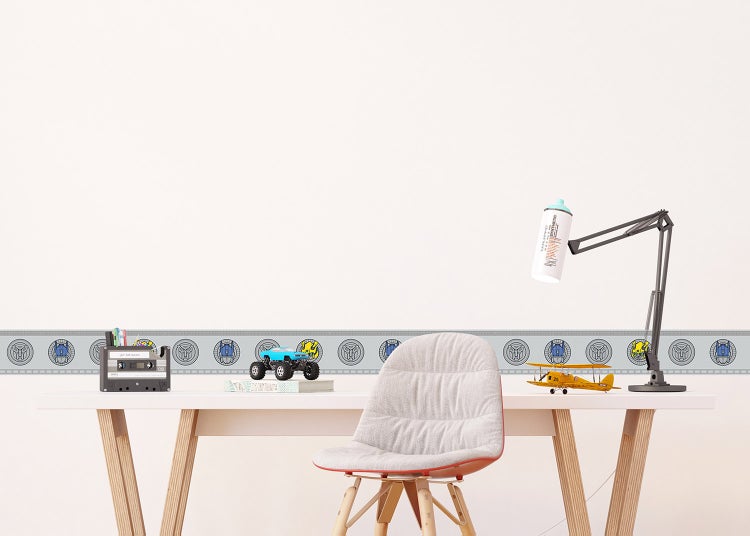 Wandbordüre mit Transformers-Motiven in einem hellen Kinderzimmer über einem Schreibtisch mit Spielzeug und Lampe.