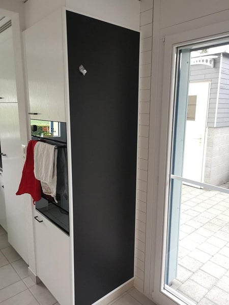 Helle Küche mit weißem Hochschrank, an dessen Seite eine schwarze, magnetische Tafelfolie angebracht ist, neben einem Backofen.