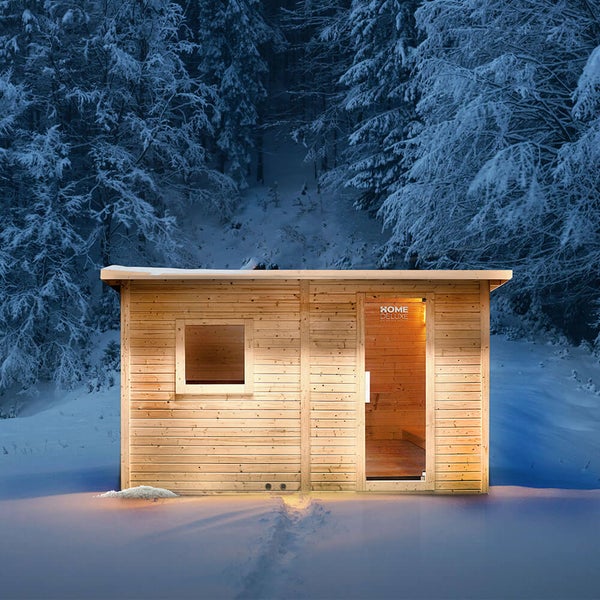 Eine Home Deluxe Gartensauna aus Holz mit Glasfront in einer verschneiten Winterlandschaft, beleuchtet mit warmem Innenlicht.