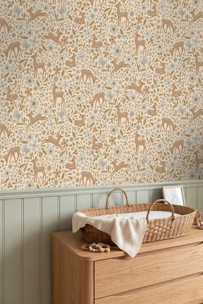 Tapete mit Reh und Blumen Muster für Kinderzimmer über einer holzfarbenen Kommode mit geflochtenem Weidenkorb als Wickelunterlage.