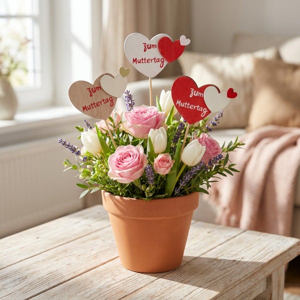 Blumenstrauß aus Rosen und Tulpen im Terrakottatopf mit herzförmigen Muttertagssteckern als Dekoration auf einem Holztisch