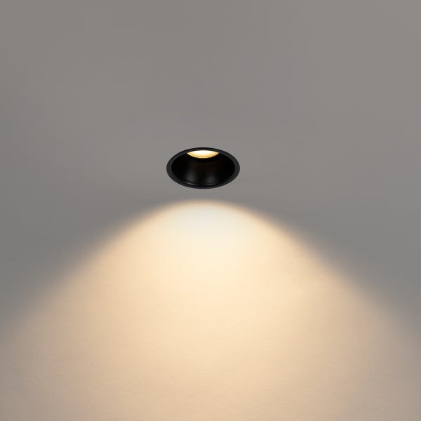 Schwarzer runder Einbaustrahler mit warmweißem Lichtkegel.