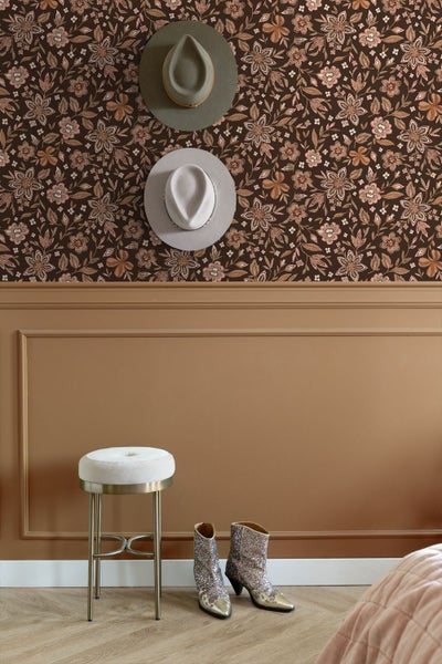 Gemütliches Schlafzimmer mit floral gemusterter Tapete, gepolstertem Samtkopfteil in Braun, rostfarbener Bettwäsche und einer Tischlampe.