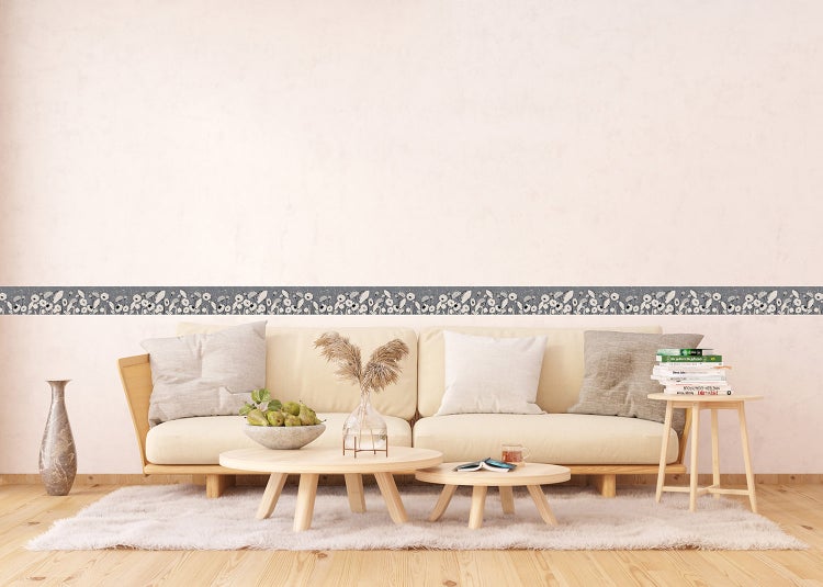 Tapetenbordüre mit floralem Muster in einem hellen Wohnzimmer mit Sofa, Couchtischen und Holzboden.