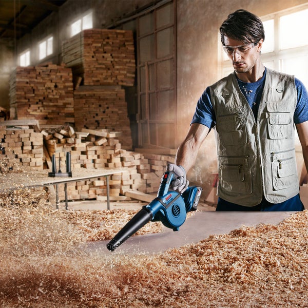 Ein Mann benutzt einen Akku-Laubbläser zum Entfernen von Holzspänen in einer Werkstatt.