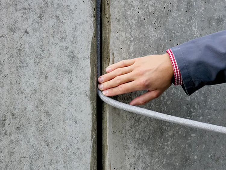 Hand drückt Fugendichtband in eine Betonfuge zur Abdichtung