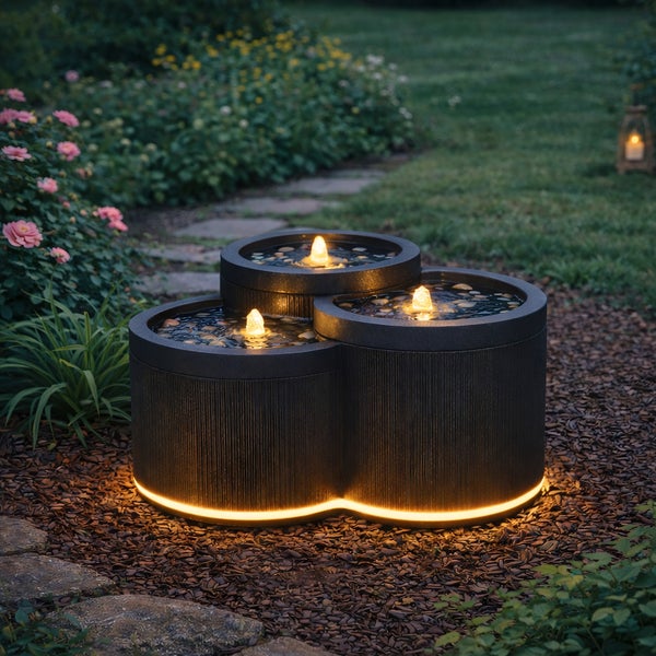 Dreistufiger Gartenbrunnen mit strukturierter Oberfläche und Beleuchtung am Boden sowie in den Wasserauslässen.