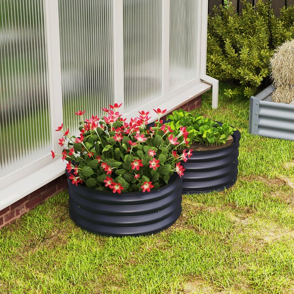 Zwei runde Hochbeete aus Wellblech im Garten, eines mit Blumen und eines mit Pflanzen bepflanzt, neben einer strukturierten Wand.