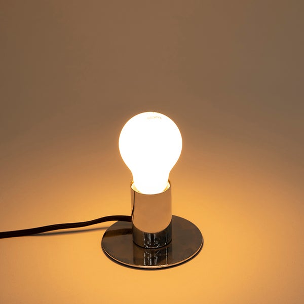 Tischleuchte mit rundem Sockel in Chrom-Optik und eingeschalteter, matter Glühbirne.