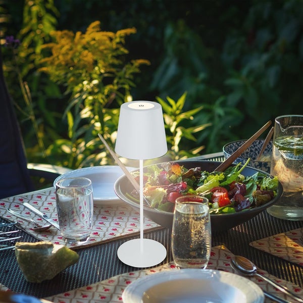 Moderne weiße LED Tischleuchte auf einem gedeckten Gartentisch mit Salat und Getränken im Freien.