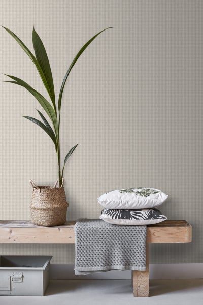 Innenraum mit einem Tisch, Kissen und einer Zimmerpflanze vor einer strukturierten Tapete
