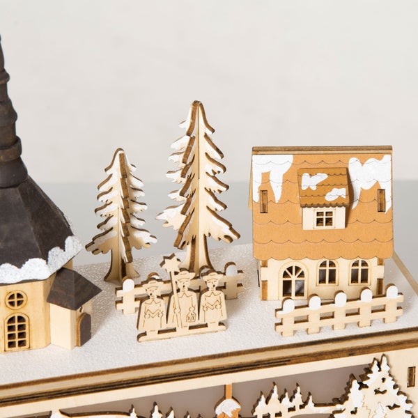 Weihnachtsdekoration aus Holz, Szene mit Kirche, Haus, Tannenbäumen und Sternsingern auf einer verschneiten Grundplatte.
