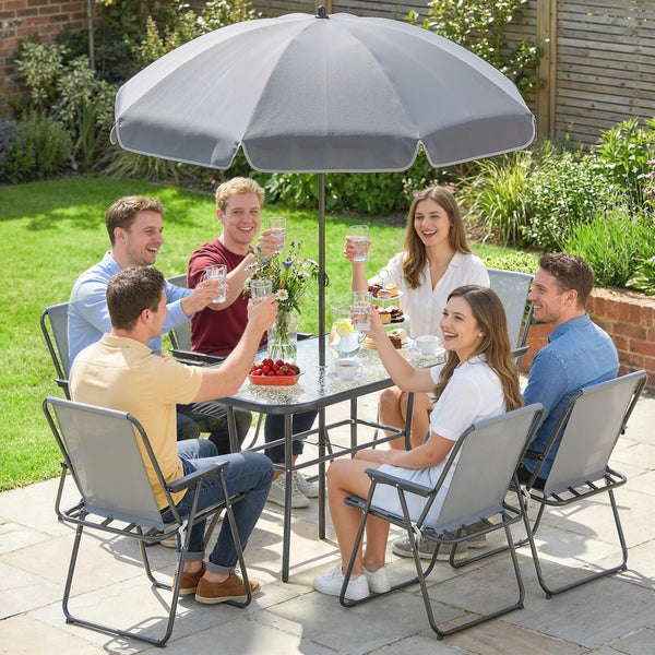 Gruppe von Personen an einer grauen Garten-Sitzgruppe mit Glastisch, sechs Klappstühlen und großem Sonnenschirm auf einer sonnigen Terrasse.