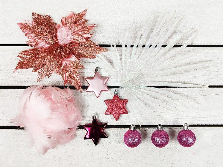 Weihnachtsbaumschmuck Set bestehend aus glitzernden Sternen, Weihnachtskugeln, einer dekorativen Blume und einem Palmwedel auf Holzuntergrund.