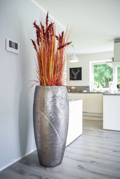 Große silberne Bodenvase mit strukturiertem Muster und hohen Trockenpflanzen in einer modern eingerichteten, hellen Küche.