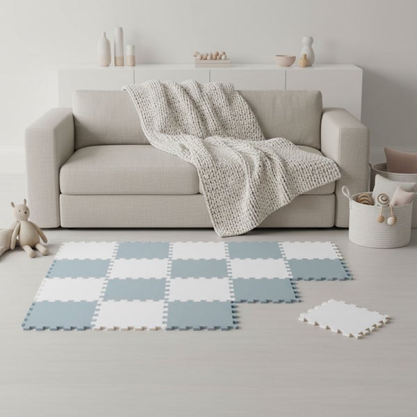 Hellblau-weiße Schaumstoff-Puzzlematte im Karo-Muster auf dem Boden eines hellen Wohnzimmers mit beigem Sofa und Strickdecke.