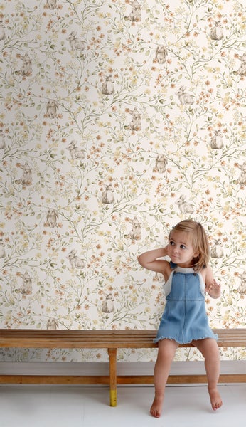 Kind sitzt vor einer Wand mit floraler Tapete mit Hasenmotiven