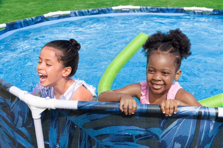 Zwei Kinder spielen in einem Aufstellpool mit Blattmuster und Poolnudeln auf einer Rasenfläche.