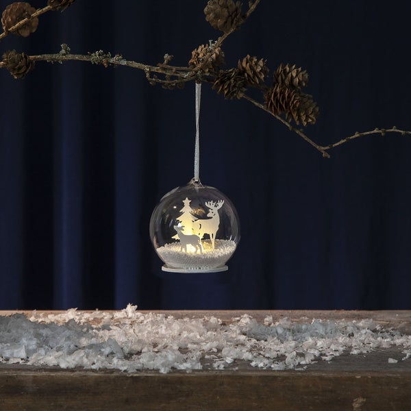 Dekorative Weihnachtskugel mit Hirsch und Baum auf einem Ast