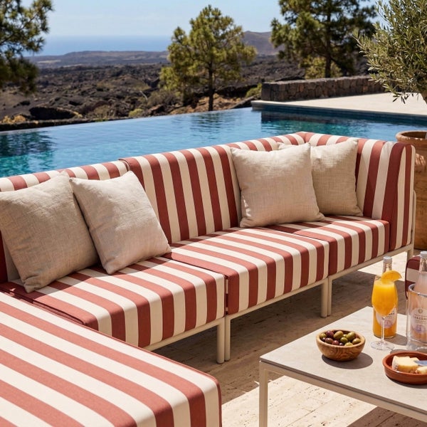 Modernes modulares Gartensofa mit rot-weiß gestreiftem Muster, hellen Kissen und Metallgestell auf einer Terrasse an einem Pool.