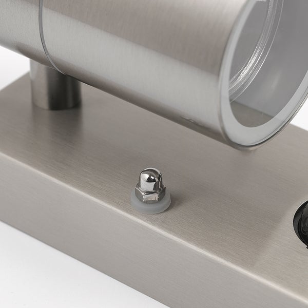 Detailansicht einer Außenwandleuchte aus Edelstahl mit zylindrischem Lampenkopf, rechteckiger Wandhalterung und Sechskantmutter.