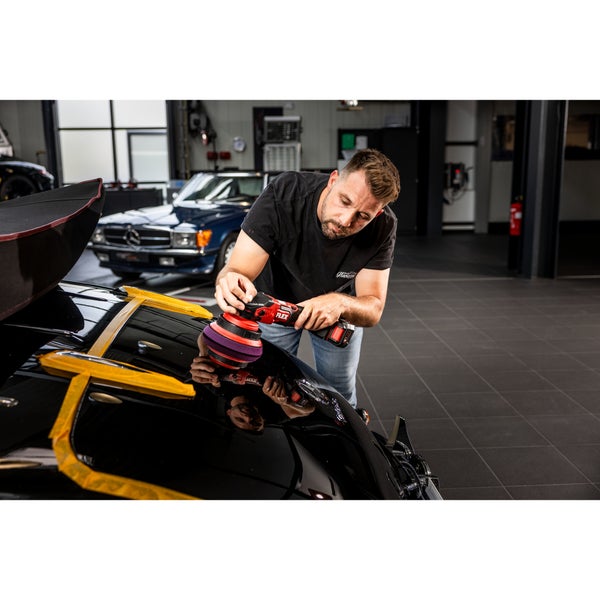 Ein Handwerker nutzt einen Akku Exzenterschleifer von Flex zum Polieren eines schwarzen Autos in einer Werkstatt.